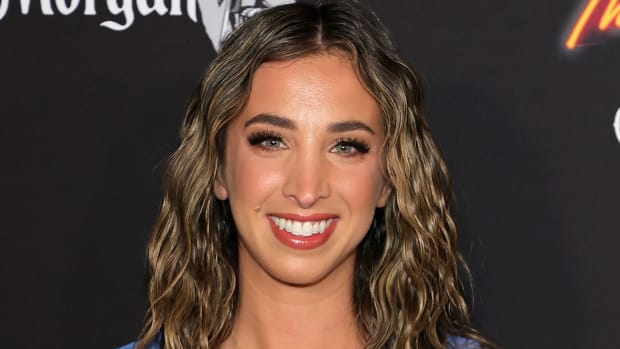 Katie Austin sports a curly down-do and a pink glossy lip and smiles for the camera.