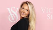Camille Kostek smiles over her shoulder, wearing a black long-sleeved dress and her long blonde hair down.