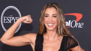 Katie Austin flexes her arm and poses for the camera in a black gown.