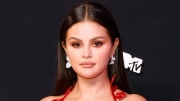 Selena Gomez poses in front of a black backdrop in a red dress.