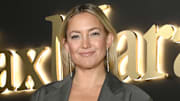 Kate Hudson poses in a gray blazer and silver drop earrings and smiles for the camera.