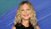 Meg Ryan poses in a black high-neck dress and sports her signature curls. She smiles for the camera.