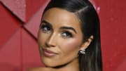 Olivia Culpo poses with her hair slicked back and smiles over her shoulder at the camera.