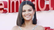 Selena Gomez poses and smiles for the camera in a silver sparkly dress and drop earrings.