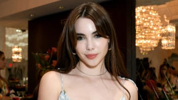 McKayla Maroney smiles for the camera wearing a baby blue and white patterned dress and her brown hair down.