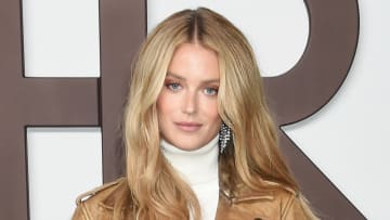 Kate Bock poses in a cream turtleneck sweater and tan leather jacket.