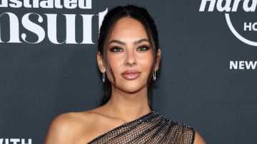 Christen Harper poses before a gray backdrop wearing a black sparkly mesh one-shoulder dress.