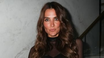 Melissa Wood-Tepperberg poses for the camera, wearing a sheer high-neck top and her brown hair in a dramatic curl.