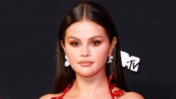 Selena Gomez poses in front of a black backdrop in a red dress.