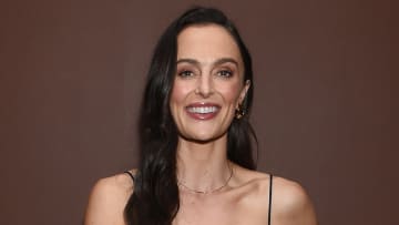 Megan Roup poses for the camera in a black dress in front of a brown backdrop.