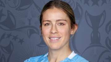 Abby Dahlkemper poses in a blue soccer jersey and smiles for the camera.