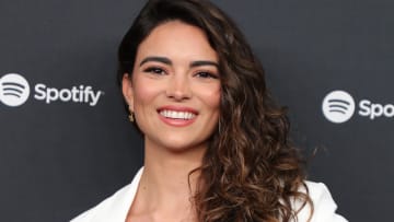 Kyra Santoro wears her brown curly hair in a down-do and smiles for the camera.
