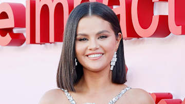 Selena Gomez poses and smiles for the camera in a silver sparkly dress and drop earrings.