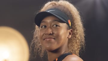 Naomi Osaka poses in a black visor and smiles into the distance.