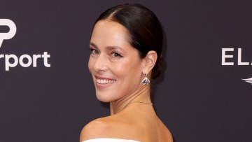 Ana Ivanovic poses in a white off-the-shoulder gown and smiles over her shoulder at the camera.