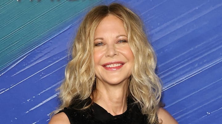 Meg Ryan poses in a black high-neck dress and sports her signature curls. She smiles for the camera.