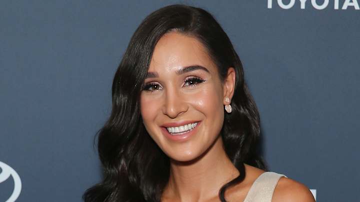 Kayla Itsines sports her black hair in a Hollywood wave and smiles for the camera.