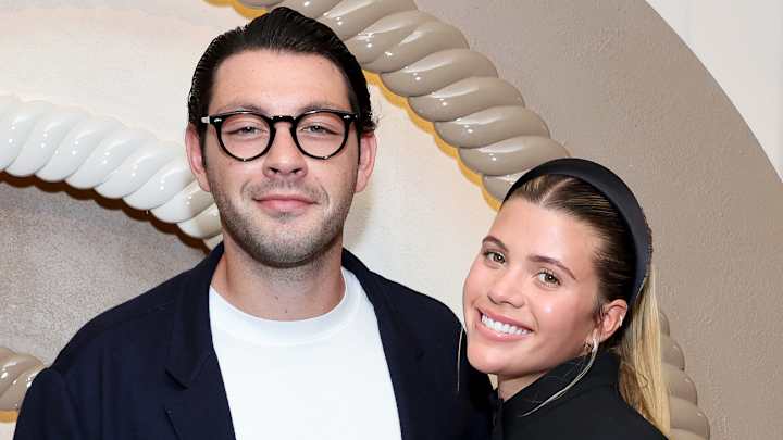Elliot Grainge and Sofia Richie pose side-by-side and smile for the camera.