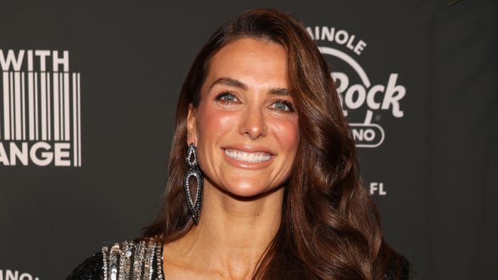 Melissa Wood-Tepperberg poses and smiles wearing a black and silver sparkly dress and matching dangle earrings.