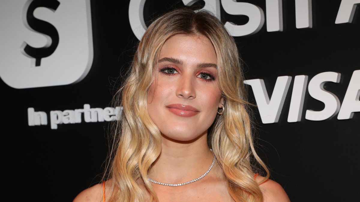 Genie Bouchard smiles softly at the camera, wearing her blonde hair down in a soft wave and a pink glossy lip.