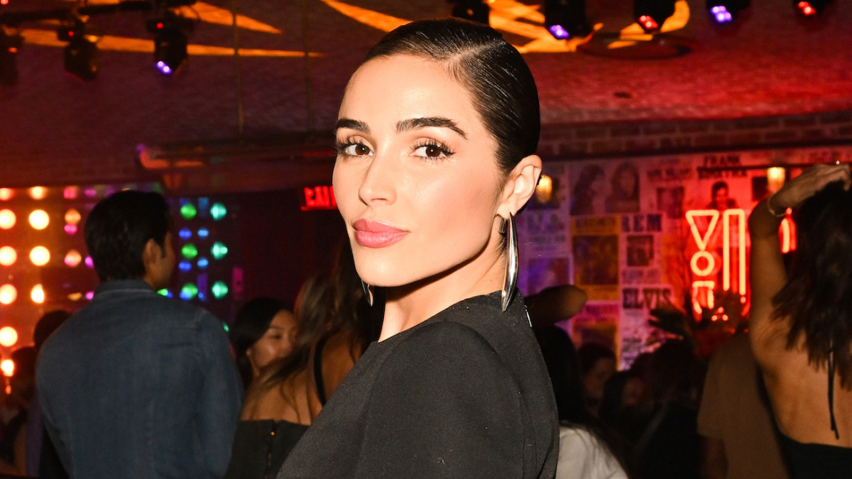 Model Olivia Culpo smiles softly at the camera sporting a slicked-back hairdo and silver drop earrings.