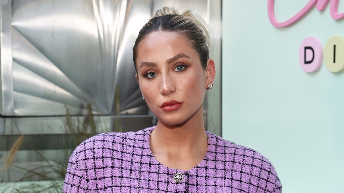 Alix Earle wears a lilac and black patterned blazer and her hair in a slicked-back bun.