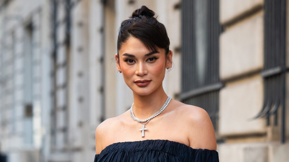 Pia Wurtzbach poses on the city street in an off-the-shoulder black dress and oversized silver cross necklace.