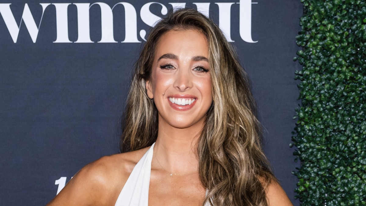 Katie Austin smiles in a white halter neck dress and her dirty blonde hair in a beach wave.