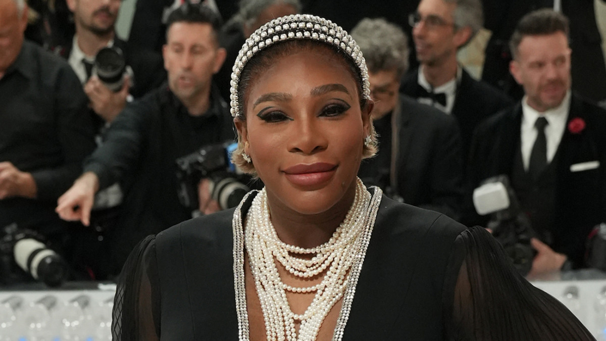 Serena Williams poses in a floor-length black gown, pearl necklaces and a pearl headband.
