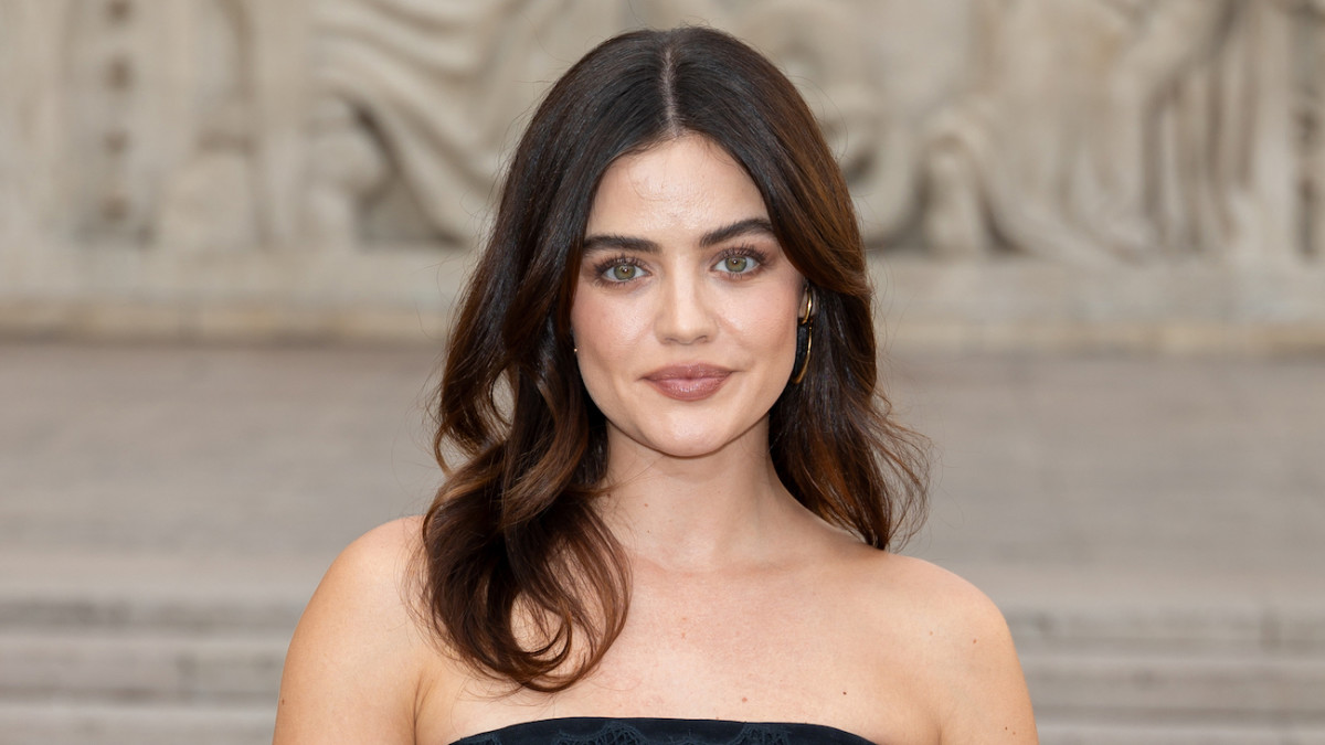 Lucy Hale wears a black strapless dress and her brown hair in a soft curl and smiles at the camera.