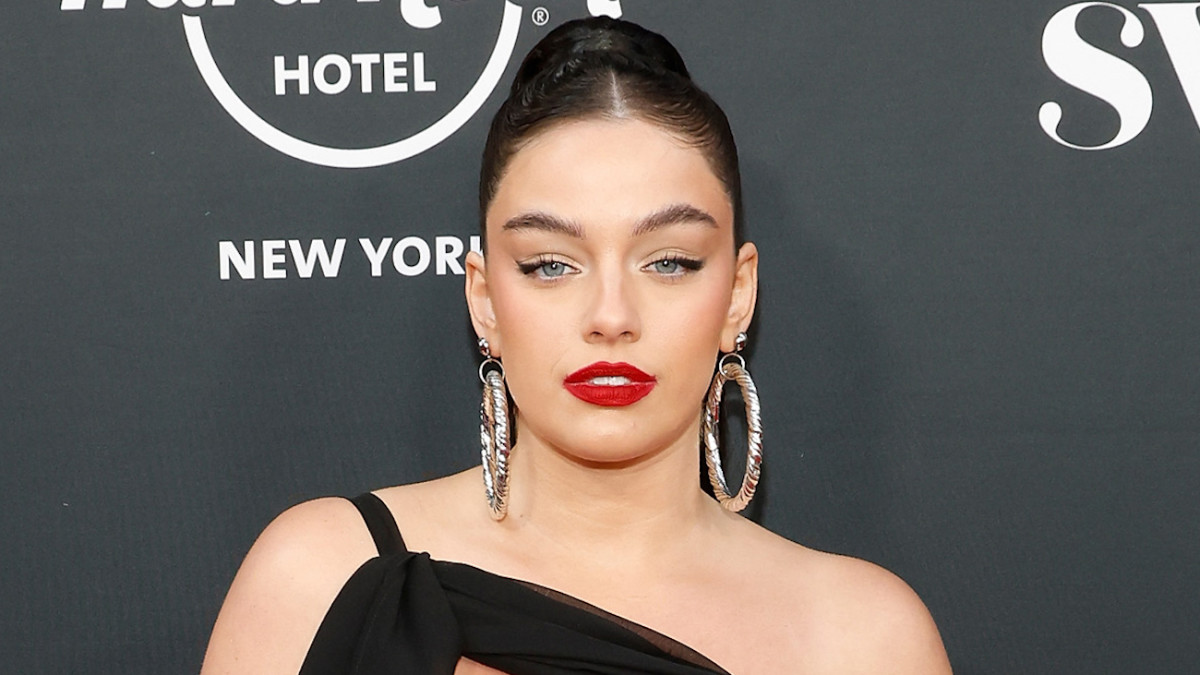 Sixtine poses in a black one-shoulder dress, oversized silver hoops and red lipstick.