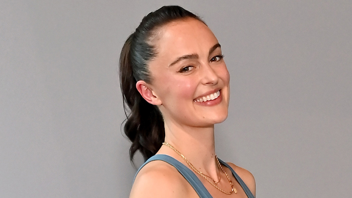 Megan Roup smiles at the camera, wearing a teal sports bra and gold necklaces.