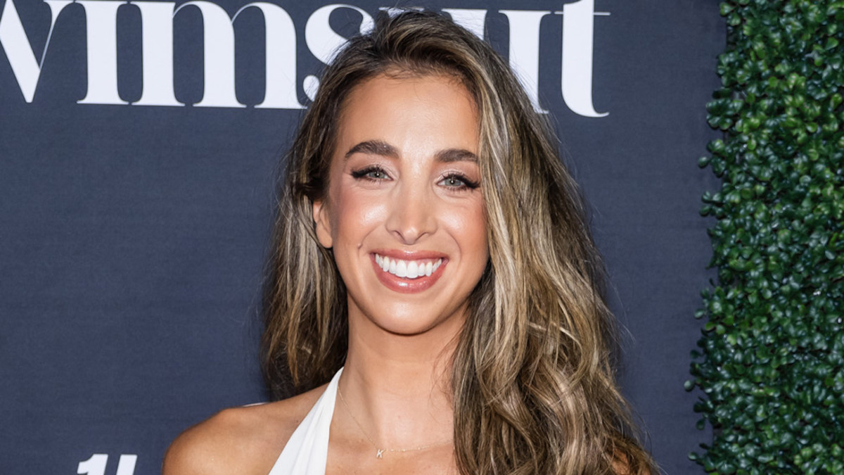 Katie Austin smiles for the camera wearing a white halter neck dress.