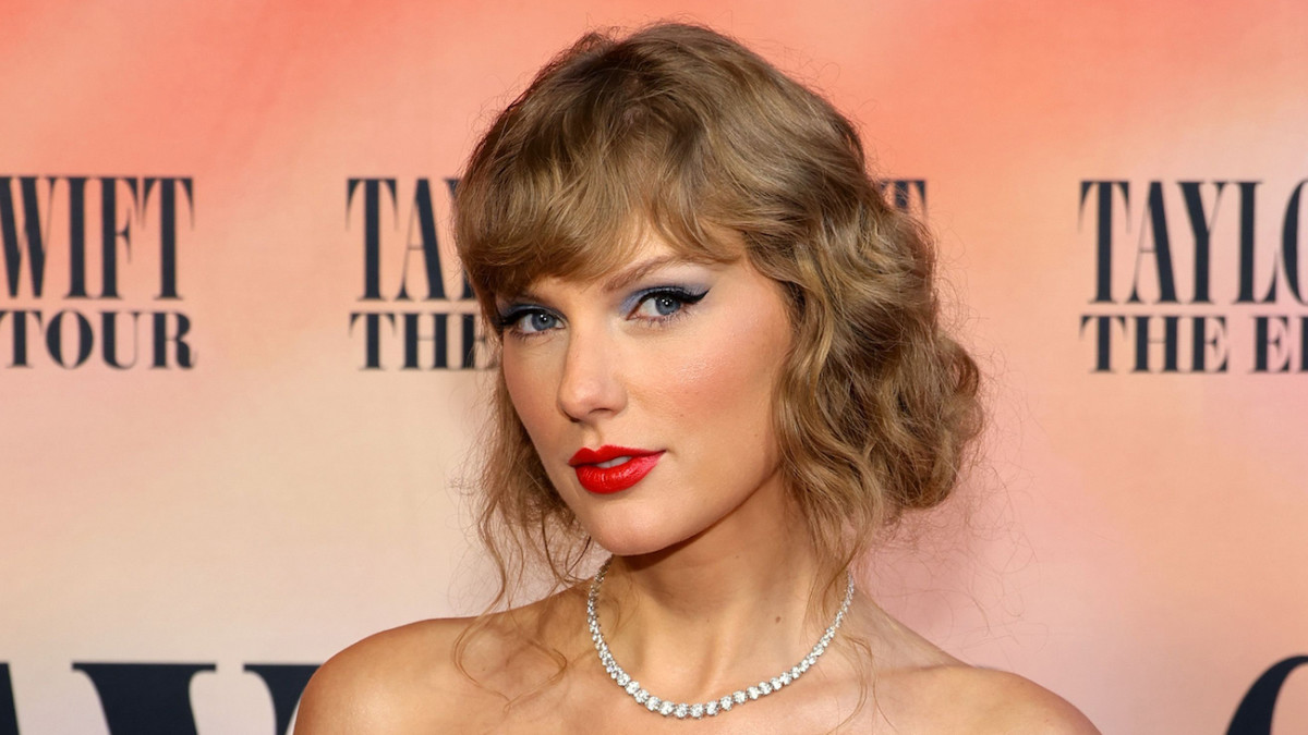 Taylor Swift poses for the camera, sporting a red lip and dramatic blue eye makeup.