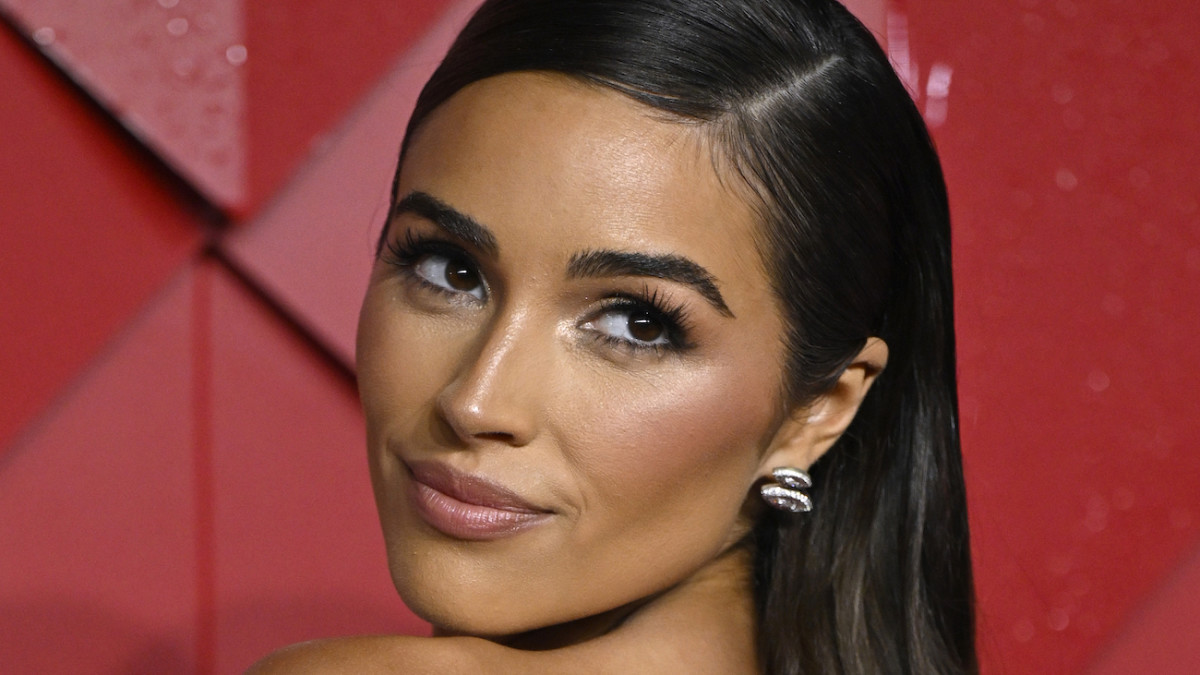 Olivia Culpo poses with her hair slicked back and smiles over her shoulder at the camera.