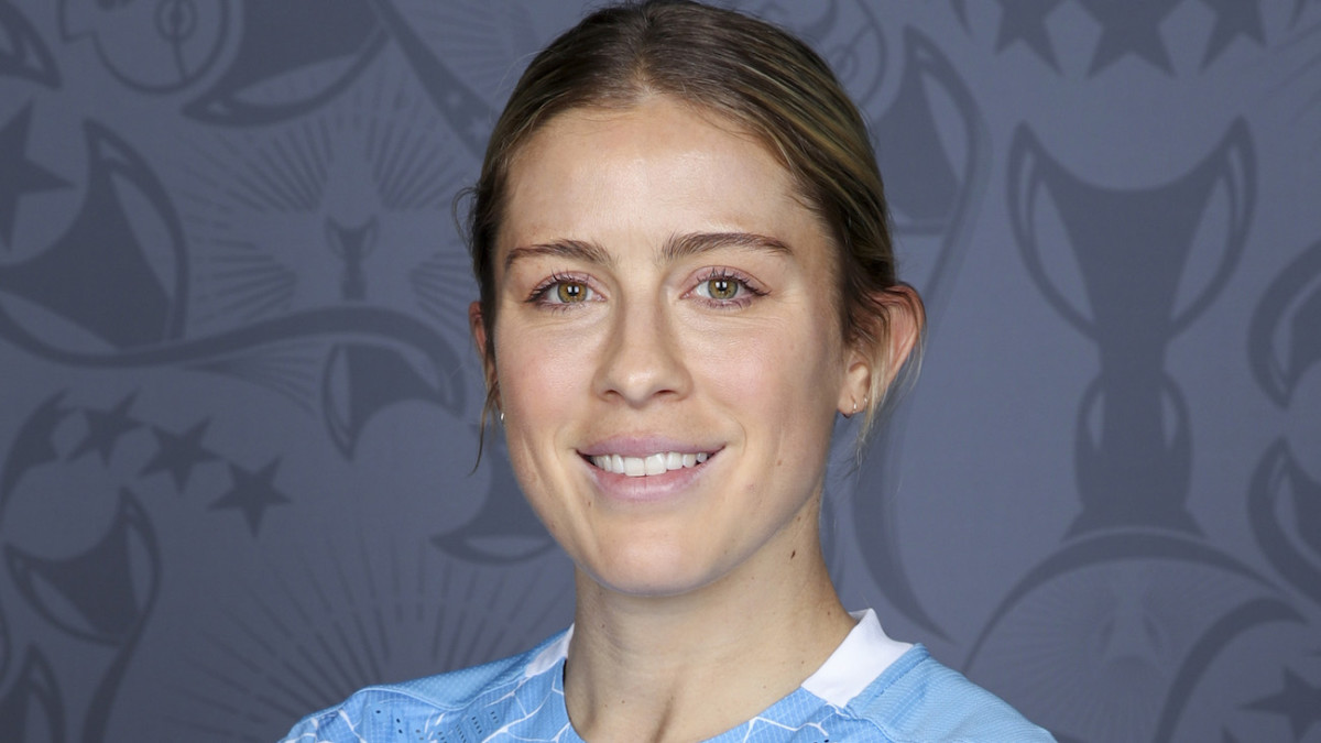 Abby Dahlkemper poses in a blue soccer jersey and smiles for the camera.