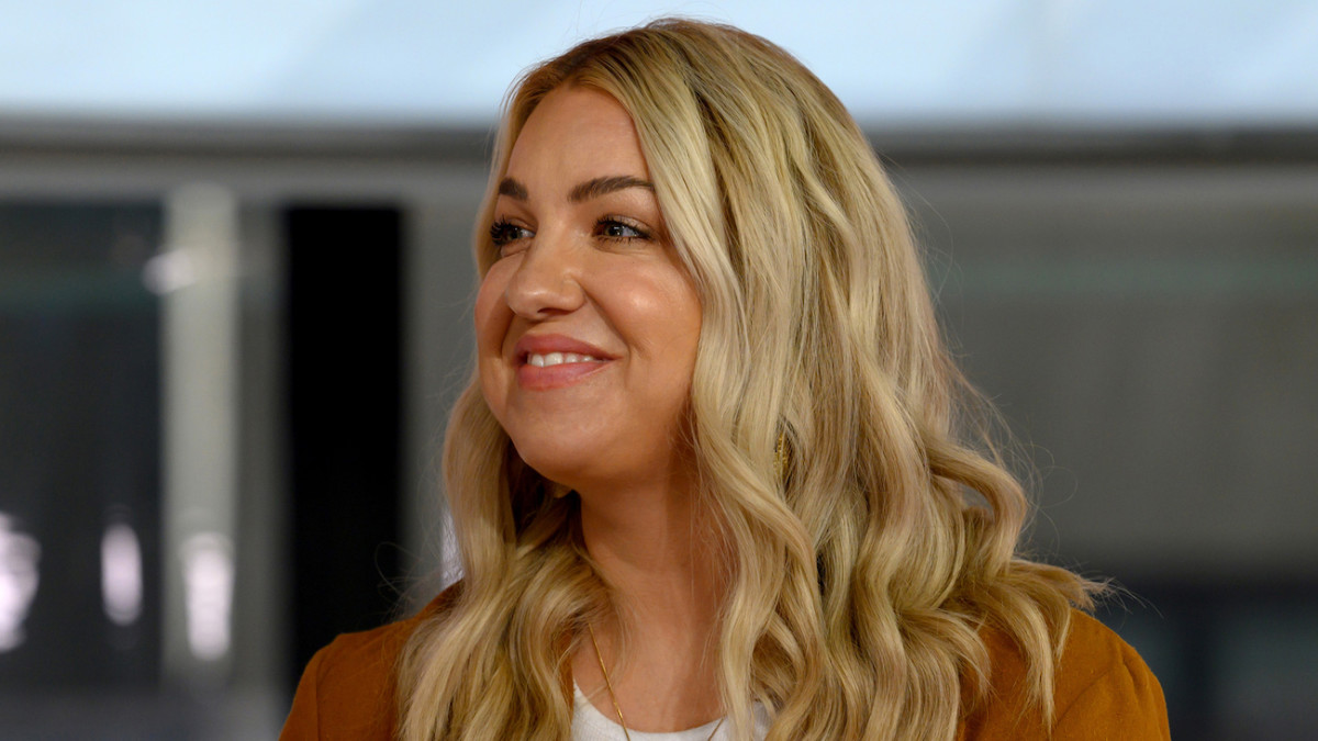 Jenna Kutcher wears a rust-colored blazer and smiles for the camera.