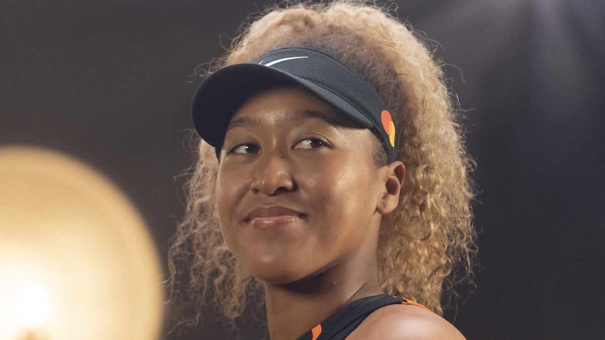 Naomi Osaka poses in a black visor and smiles into the distance.